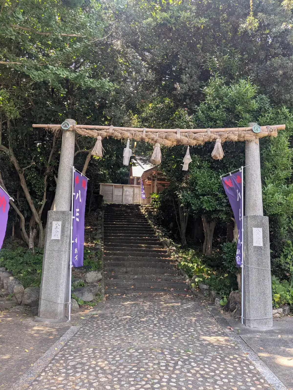 注連縄のかかった八王子社の鳥居と、紫の幟、参道の石段